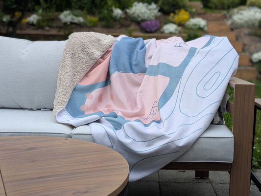 Communication blanket with the emotional regulation (see-think-feel-need) framework shown draped over a couch, in pink.