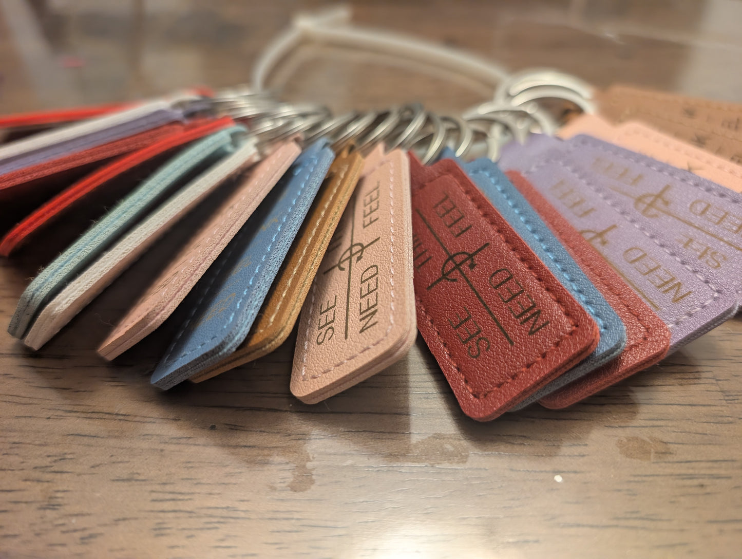 Set of colorful leather keychains with text on a wooden surface, shown in pink, red, blue, purple, and neutral colours. Communication tool printed in the design.