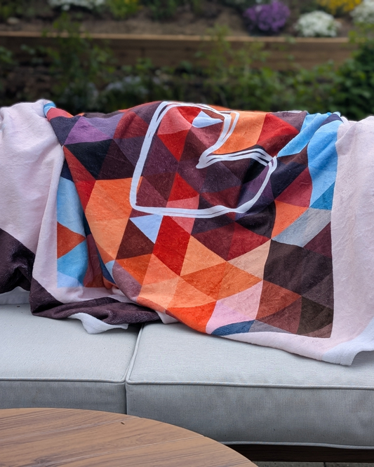 Colorful geometric-patterned communication blanket draped over a couch outdoors. The blanket features a communication tool printed in the design. 