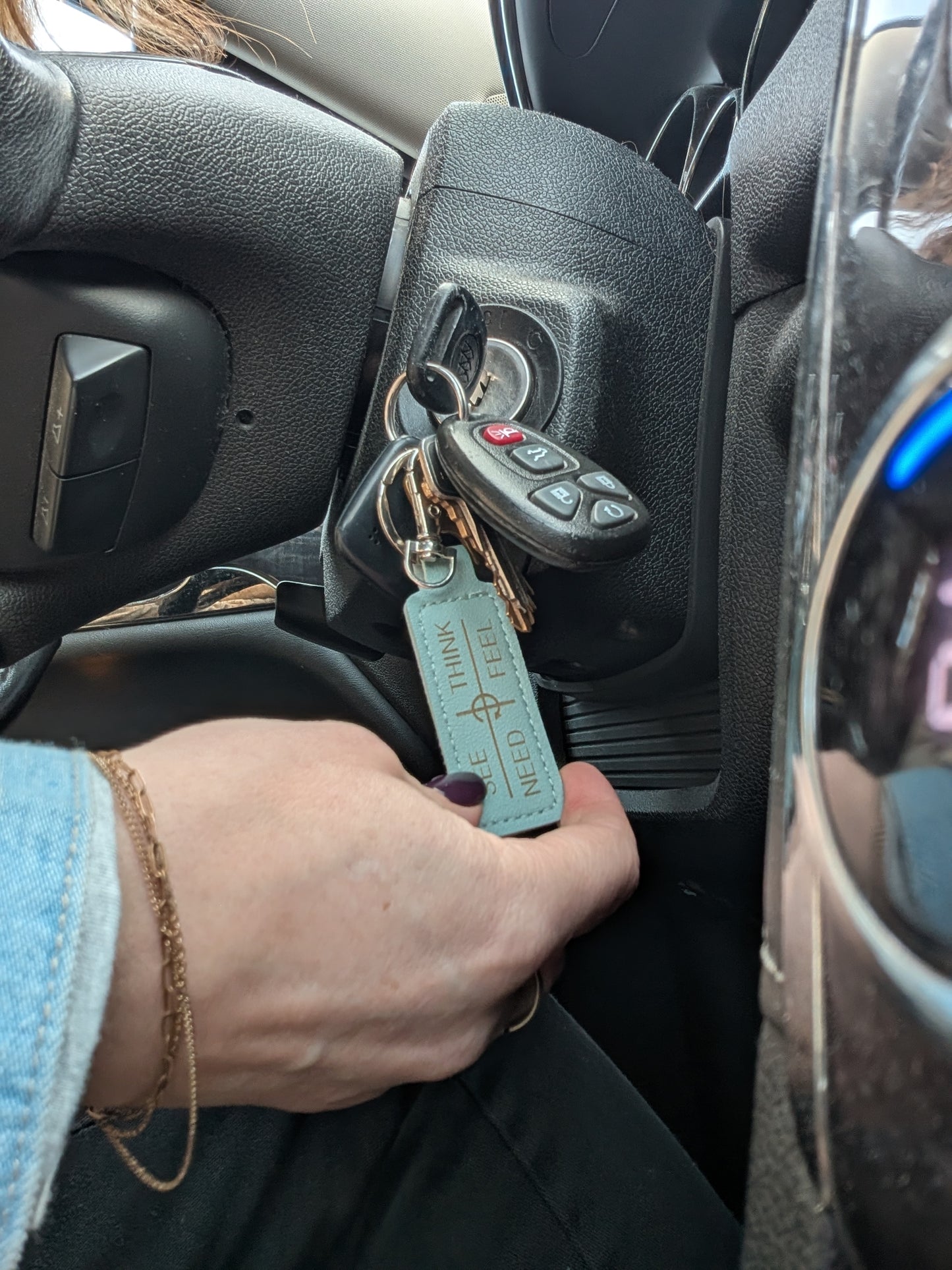 Person holding car keys with a keychain in a car's ignition area. Keychain has see-think-feel-need communication framework printed on it. 