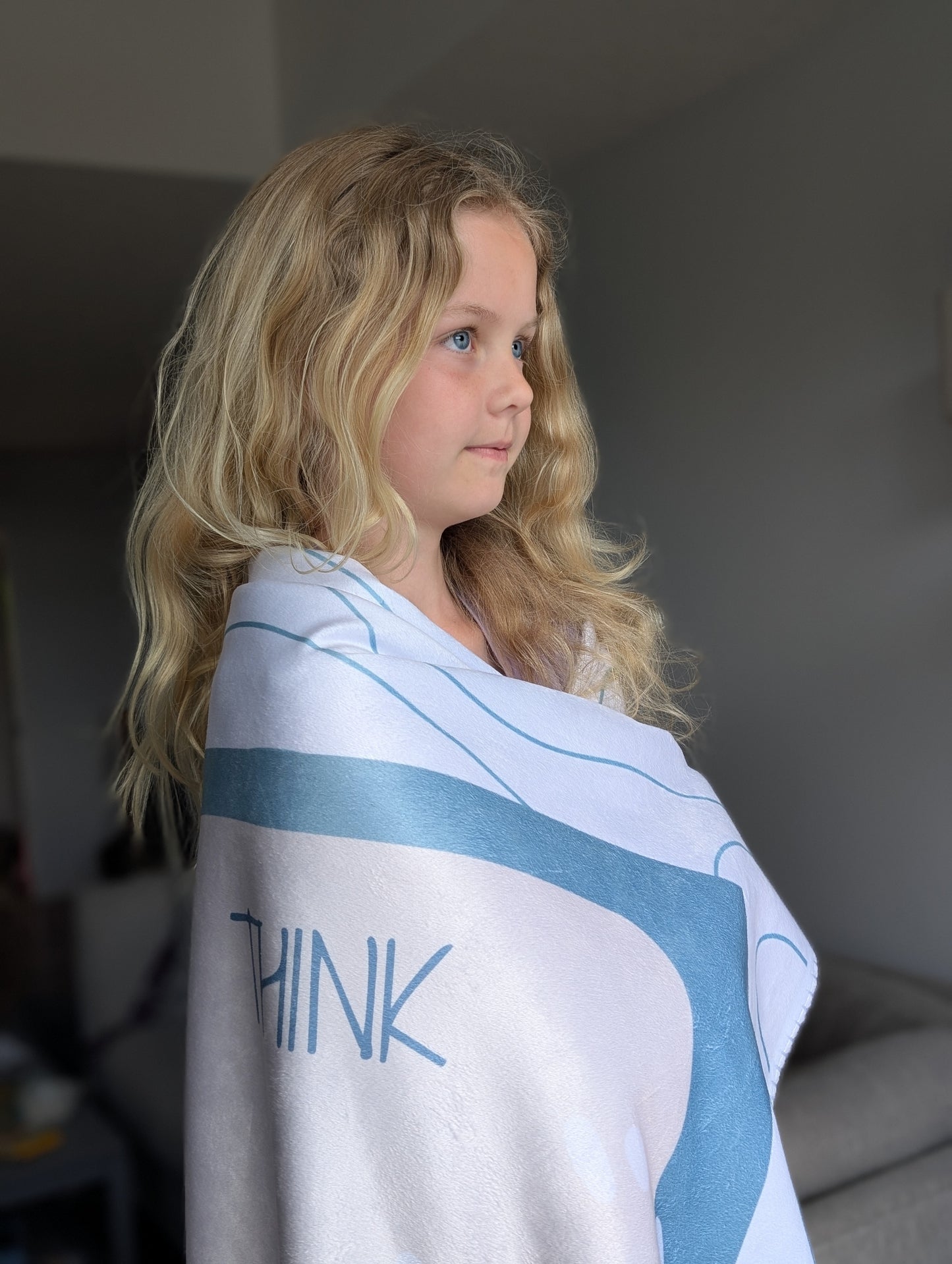 Communication blanket with the emotional regulation (see-think-feel-need) framework shown wrapped around a child. 